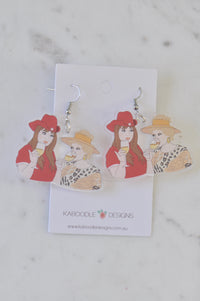 Acrylic drop earrings featuring illustrated Kath and Kim characters holding wine glasses, shown on card