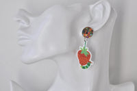 Close-up of caterpillar and strawberry acrylic earring worn on ear, showing glitter stud and charm