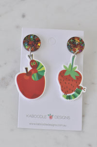 Mismatched acrylic earrings on card, caterpillar on an apple and on a strawberry with glitter star studs