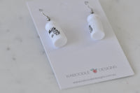 Milk bottle earrings on card angled to show glossy white finish and cow print