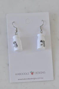 Pair of white resin milk bottle drop earrings with cow label, shown on card