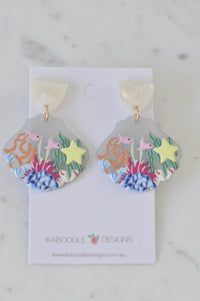 Pair of shell-shaped resin earrings with coral, fish and starfish design on white card