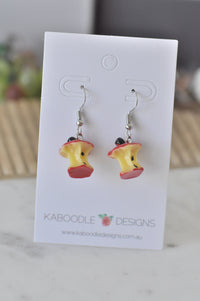 Pair of resin apple core drop earrings on Kaboodle Designs card, showing seeds and red skin