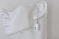 Close-up of milk bottle earring worn on ear, showing bottle shape and label