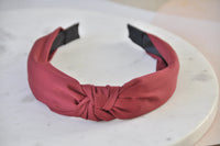 Burgundy red knotted fabric headband shown front-on with black interior edge