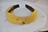 Mustard yellow fabric headband with knotted front detail on marble surface