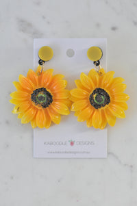 Pair of yellow resin sunflower drop earrings on a Kaboodle Designs card