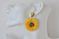 Close-up side view of sunflower earring worn on a display ear, showing dangle length