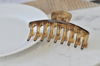 Large transparent brown acrylic claw clip shown open on a white plate, side view