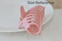Pink claw clip shown from above for size reference against a white plate