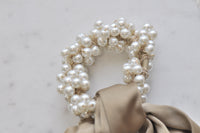 Close-up of faux pearl cluster detail on scrunchie with beige bow tail behind