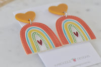 Angled view of rainbow drop earrings showing glossy resin finish and heart detail
