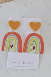 Pair of resin rainbow dangle earrings with mustard heart studs on jewellery card