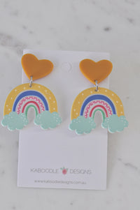 Pair of resin rainbow dangle earrings with mustard heart studs on a Kaboodle Designs card