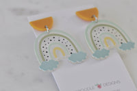 Angled view of two rainbow earrings with speckled detail and cloud charms on backing card