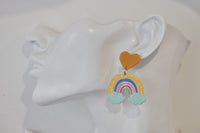 Close-up of rainbow cloud earring worn on ear showing mustard heart stud and dangle