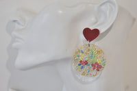 Close-up of single earring on ear showing red heart stud and floral resin disc