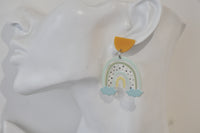 Close-up of rainbow drop earring worn on ear showing sage green arches and blue clouds