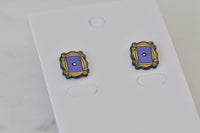 Overhead view of two frame stud earrings showing gold scrollwork detail and doorknob