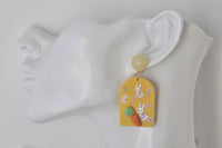 Mustard bunny carrot drop earring worn on ear, side view against plain background