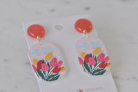 Pair of oblong acrylic earrings with pink, red and yellow tulip design, flat lay view