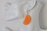 Resin mandarin segment earring shown on ear for scale