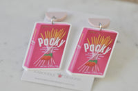 Angled view of two Pocky strawberry drop earrings on display card showing glossy acrylic finish