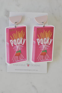 Pair of acrylic Pocky strawberry box drop earrings on pink half-moon studs, front view on card