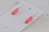 Close-up angled view of pink pencil earrings showing glossy resin finish