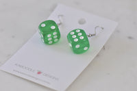 Close-up angled view of two green dice earrings with white dot detail