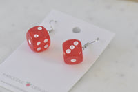 Pair of translucent red dice drop earrings with white pips on a Kaboodle card