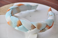 Close-up angle of blue, white and orange braided fabric headband on a marble dish
