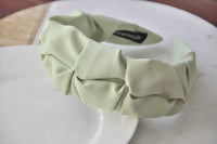 Close-up top-down view of pastel green ruffled headband showing fabric folds and interior label