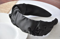 Black fabric ruffled statement headband shown at an angle, propped on a white bowl