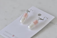 Close-up of one happy pill earring showing pink and white capsule with winking smile