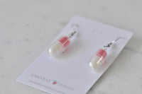 Pair of capsule-shaped earrings resting on marble surface, showing silver ear hooks