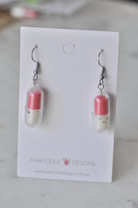 Pink and white acrylic capsule earrings with smiling faces on a Kaboodle Designs card