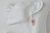 Close-up of pink happy pill earring worn on ear, showing winking smiley face