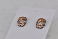 Close-up angled view of enamel stud earrings showing screaming boy face detail and black outline