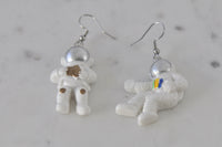 Front view of two astronaut earrings on white marble surface showing full figure and hooks