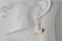 Close-up of single duck earring worn on ear showing silver hook and glossy finish