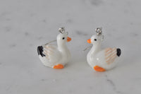 Pair of white resin duck drop earrings with orange bills and feet on marble surface