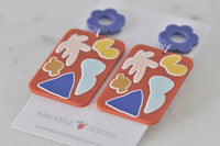 Angled view of coral resin drop earrings showing white-outlined pattern detail