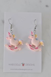 Pair of pastel pink unicorn rocking horse resin drop earrings on card backing