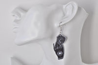 Single black Ouija hand earring with eye design worn on ear, close-up