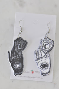 Black and white mystic hand Ouija earrings with eye and moon symbols on card