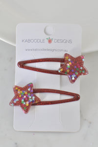 Two red glitter resin barrette clips with multicolour star confetti detail, shown on Kaboodle Designs card