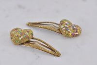 Close-up angled view of gold glitter heart clips showing resin finish and snap fastening