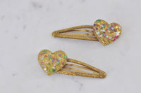 Pair of gold glitter heart hair clips with rainbow star confetti on marble surface