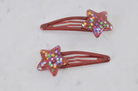 Close-up of red star barrette clips on a marble surface showing glitter and star confetti finish